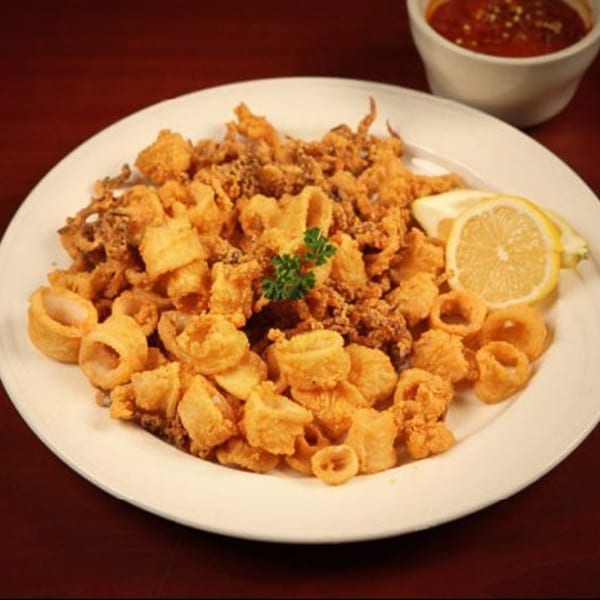 A white plate piled high with crispy fried calamari, garnished with parsley and lemon wedges.