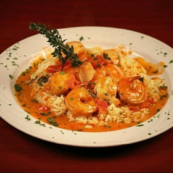 Shrimp and scallops in a rich tomato sauce with rice, garnished with fresh thyme.