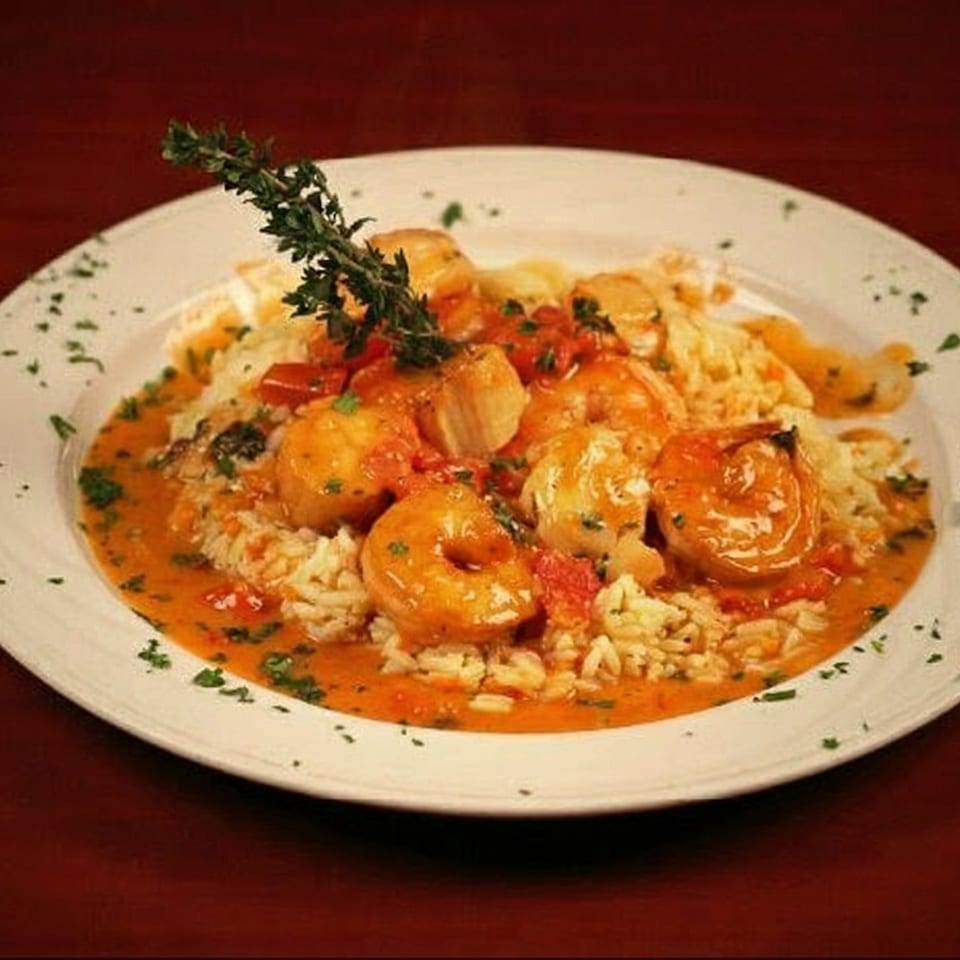 Shrimp and scallops in a rich tomato sauce with rice, garnished with fresh thyme.