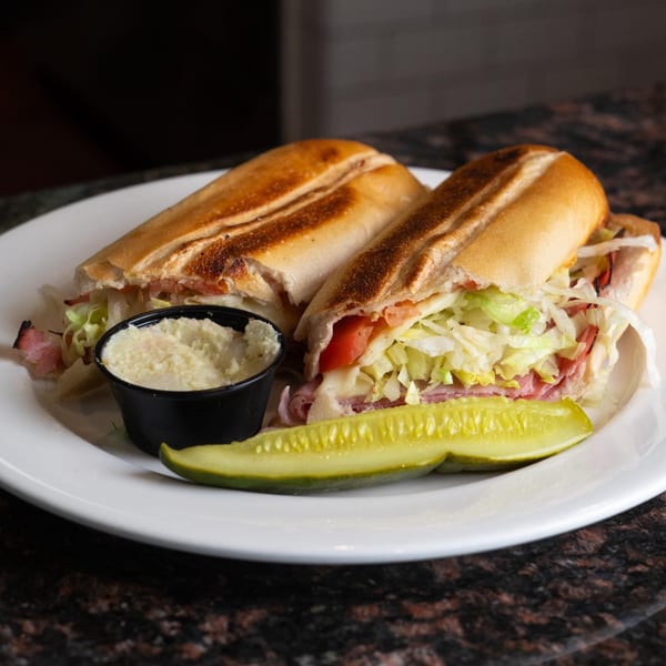 Two halves of a deli sub sandwich with lettuce, tomato, and meat, served with a pickle and coleslaw.
