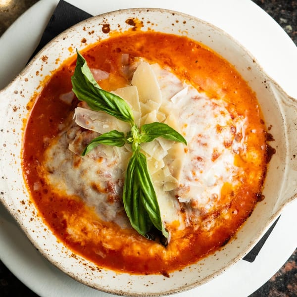 A close-up of baked lasagna in a white dish, topped with melted cheese, fresh basil, and tomato sauce.