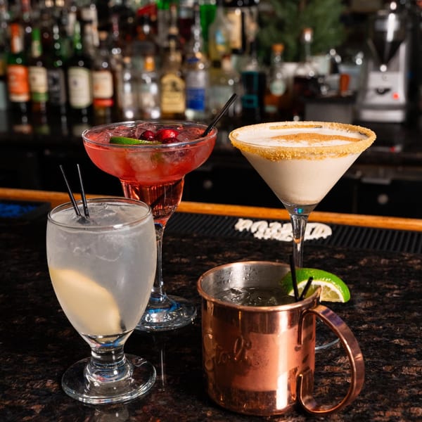 Four cocktails, including a red margarita, a creamy martini, a clear drink, and a Moscow Mule.