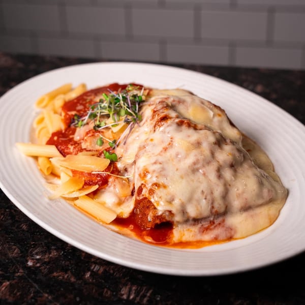 Chicken parmesan with penne pasta, red sauce, melted cheese, and microgreens on a white plate.