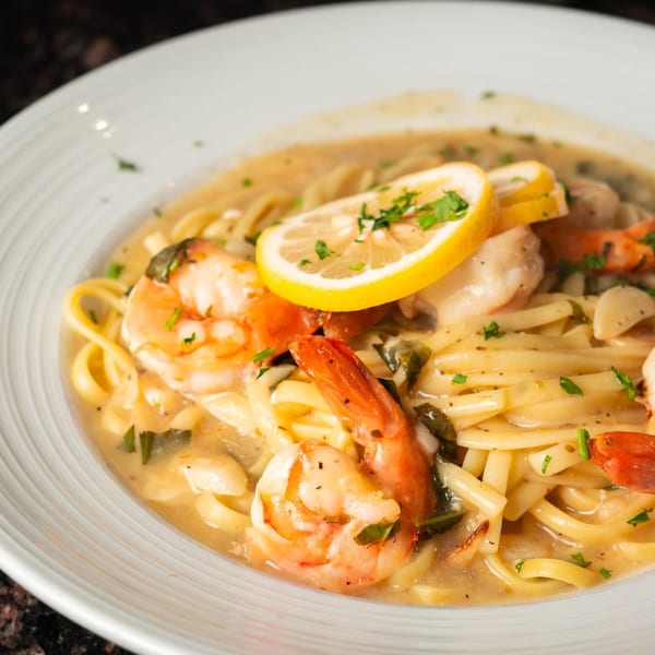 Shrimp scampi with linguine pasta, lemon slices, and fresh herbs in a white bowl.