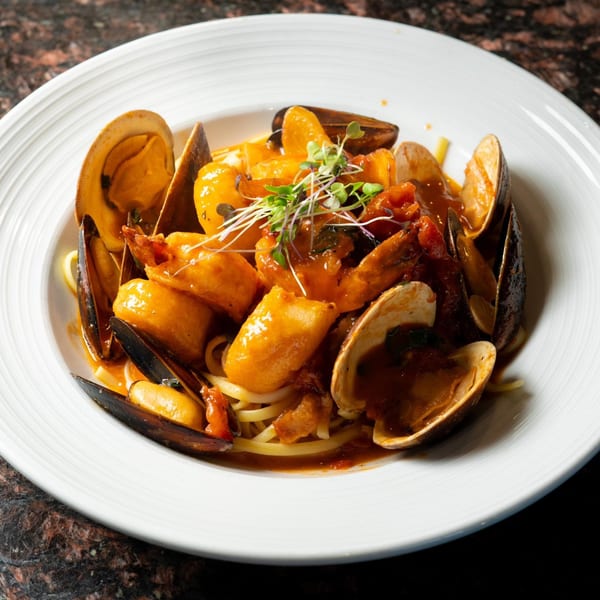 Seafood pasta with mussels, clams, shrimp, and scallops in a rich red sauce, garnished with microgreens.