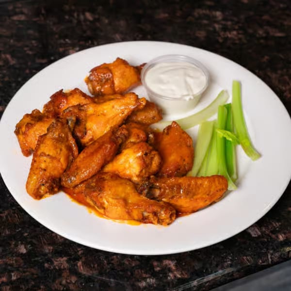 Plate of buffalo chicken wings with celery sticks and a side of ranch dressing.