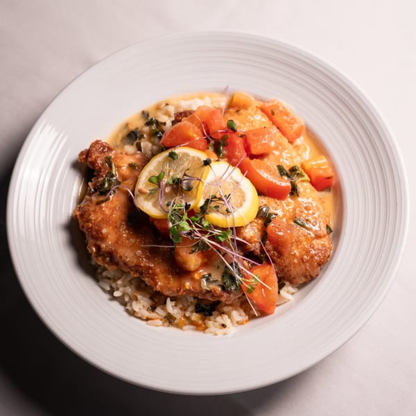 Chicken dish with rice, diced tomatoes, lemon slices, and microgreens in a white bowl.