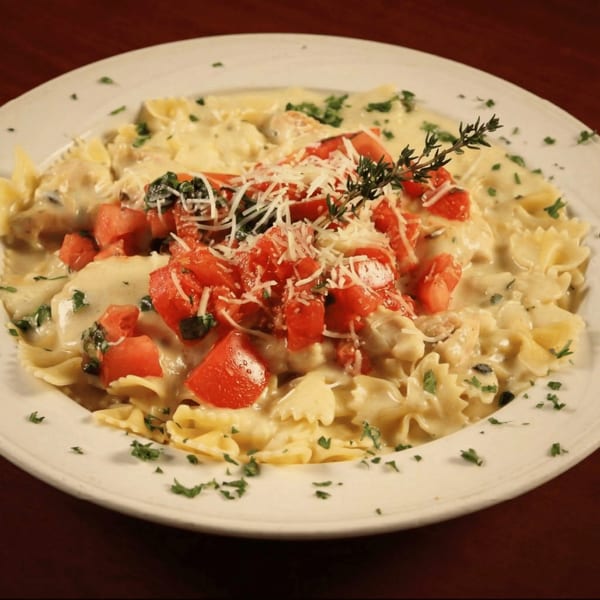 Creamy pasta with bow-tie noodles, diced tomatoes, grated cheese, and fresh herbs on a white plate.